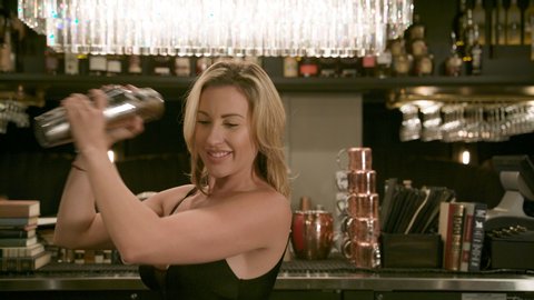 Smiling Blond Female Bartender Shakes Cocktail at Bar in Slow Motion