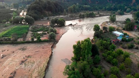 Aerial drone shot; fly over flooding along the muddy flowing river, inundated rural houses and agricultural fields,mired car arounds