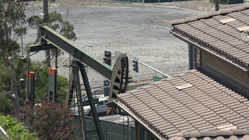 An oil pump jack working beside the roof of a residential home