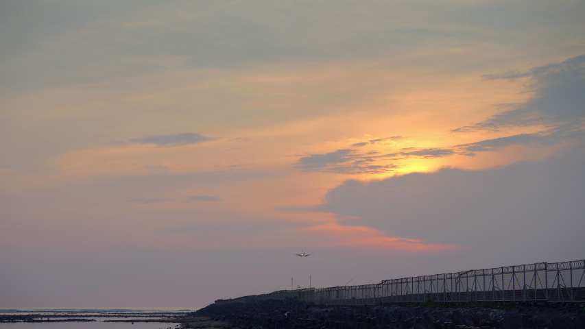 Civil airplane with head lights is landing on runway near tropical beach in yellow sunset with sun behind