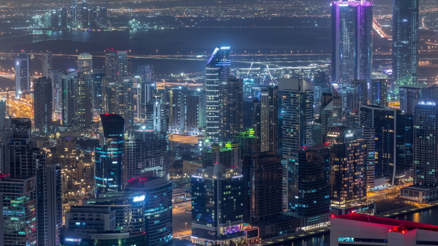 Panoramic aerial view of business bay towers in Dubai night timelapse. Rooftop view of some illuminated skyscrapers, canal and new towers under construction. | Shutterstock HD Video #1034891423