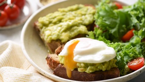 Poached egg on rye bread toast with avocado and green leaf salad kale. Healthy food, clean eating concept. Closeup