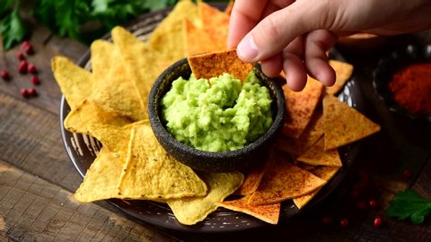Male hand dipping corn chips nachos into guacamole. Eating mexican food, snack or appetizer