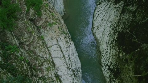 The flight of the drone over a mountain gorge through thickets of greenery, in which flows a mountain, turbulent and winding river