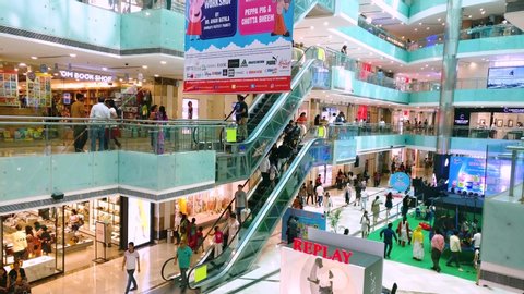 Gurgaon, Delhi, India - circa 2019: people moving down an escalator in a busy shopping mall in gurgaon delhi with lots of branded shops and events happening. Shows the events happening in the lobby