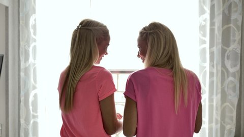 Two blondes in pink clothes sprinkle muffins with powdered sugar, sifting through a sieve, view from the back