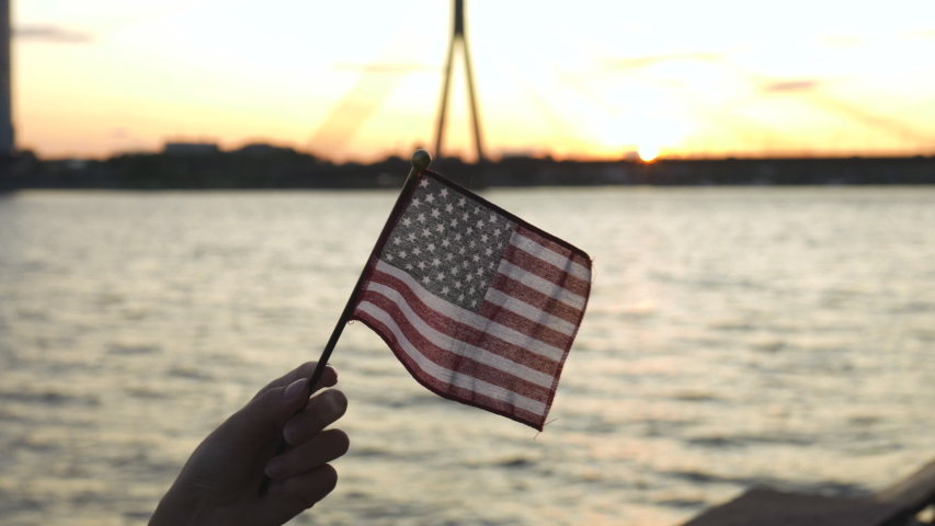 Hand flutters USA American Flag isolated in the sunset by the river