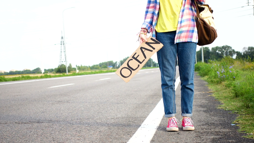 Young girl with a guitar coming along the road and hitch-hiking
