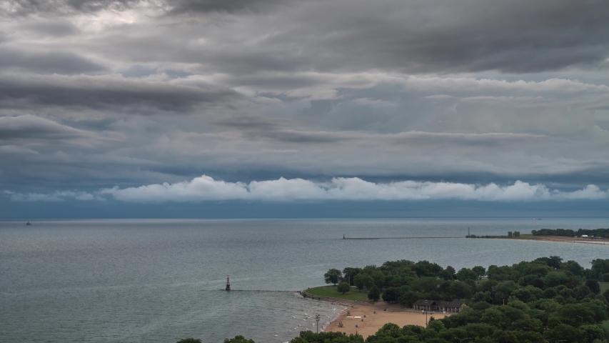 Time lapse of low lying fluffy white clouds passing over the horizon below higher storm clouds as they dissipate as the sun rises and shines through beyond in the morning over Lake Michigan in Chicago