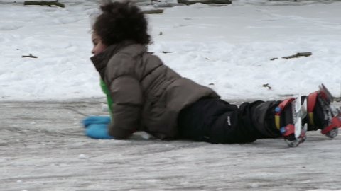 Amsterdam, January 6, 2012. A cute little dark girl runs on her ice skates and falls on the ice in a park, then smiles.