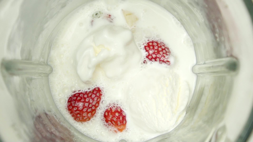 Closeup shot of milk, fruit, and ice cream mixing together in a blender.