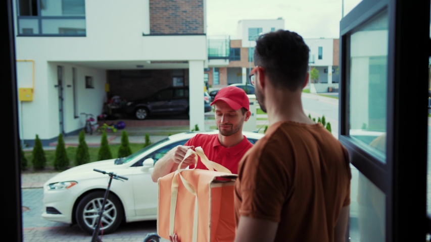 Positive delivery guy taking out lunch bag to the customer standing in door. Close-up happy handsome man receiving fresh food giving high five to delivery man. Modern delivery service. Royalty-Free Stock Footage #1034918825