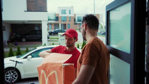 Positive delivery guy taking out lunch bag to the customer standing in door. Close-up happy handsome man receiving fresh food giving high five to delivery man. Modern delivery service.