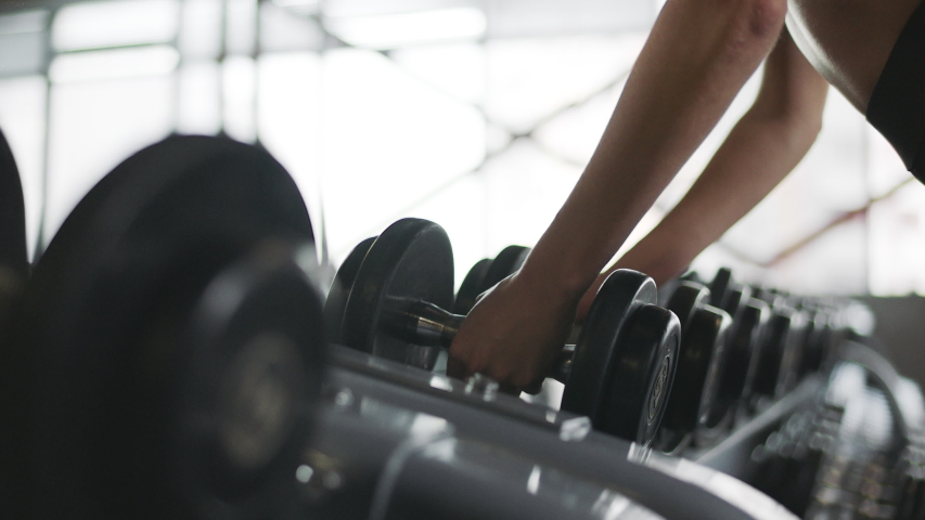 Female hands taking bodybuilding dumbbells in gym club. Closeup woman hands taking weight lifting in sport club. Fitness girl having sport training in fitness gym. | Shutterstock HD Video #1034920292