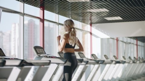 Fitness woman running on treadmill in gym. Athlete woman using run machine in fitness center. Pretty girl having cardio training in sport club.