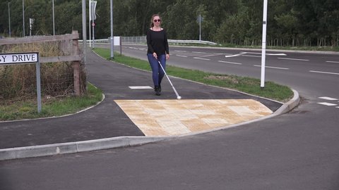 Young woman using long cane to cross a road