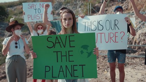 Young activists in action against pollution stay at landfill site. Focus on young woman holding climate strike poster at protest strike. Save the Planet.
