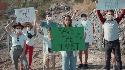Save environment protest. Group of young people fighting against earth trash pollution staying at dump. Focus on charming smart woman showing agitation sign Save the Planet.