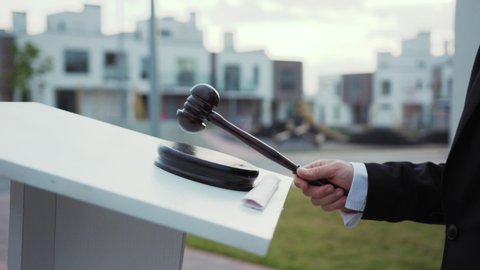 Property auction on real estate. Close-up auctioneer banging with mallet gavel by tribune outdoors. Auction bid sale jughment.