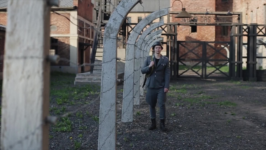 A close view of a young male actor dressed as a German soldier near a barbed wire fence guarding a death camp