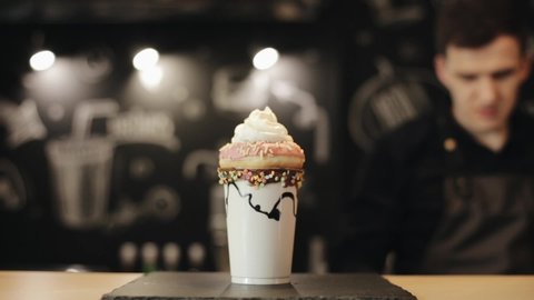 A male barista hand sprinkling confectionary dressing over milkshake with donut and whipped cream