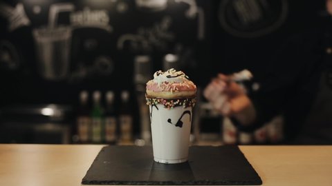 A male barista putting a chocolate wafer bar in a crazy milkshake with a donut and whipped cream