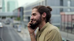 Smiling man talking by smartphone. Side view of handsome happy young man talking by mobile phone on street. Communication concept