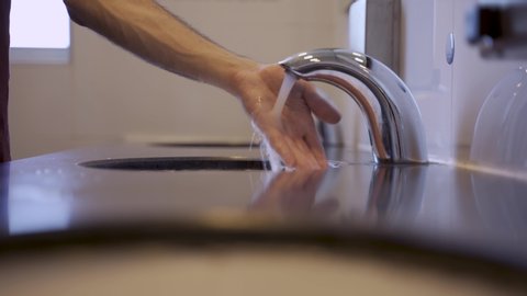 Man washing hands in public toilets with touch-less faucet or tap