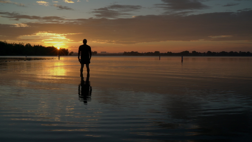 sunrise silhouette of a senior man standing in shallow water and  practicing chigong breathing and movements, Boyd Lake State Park in northern Colorado