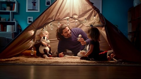 Dad with daughters in a tent at home. Dad imitates a penguin.