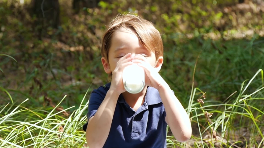 A happy child in nature loves to drink kefir from a dairy product from a transparent glass cup in slow motion Royalty-Free Stock Footage #1034963294