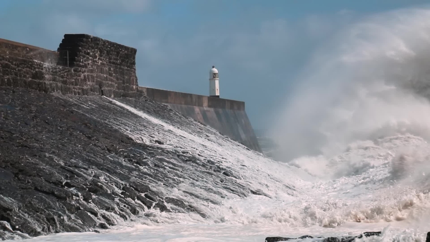 Huge ocean waves and surf crashing against a sea wall and lighthouse (Porthcawl, South Wales)
