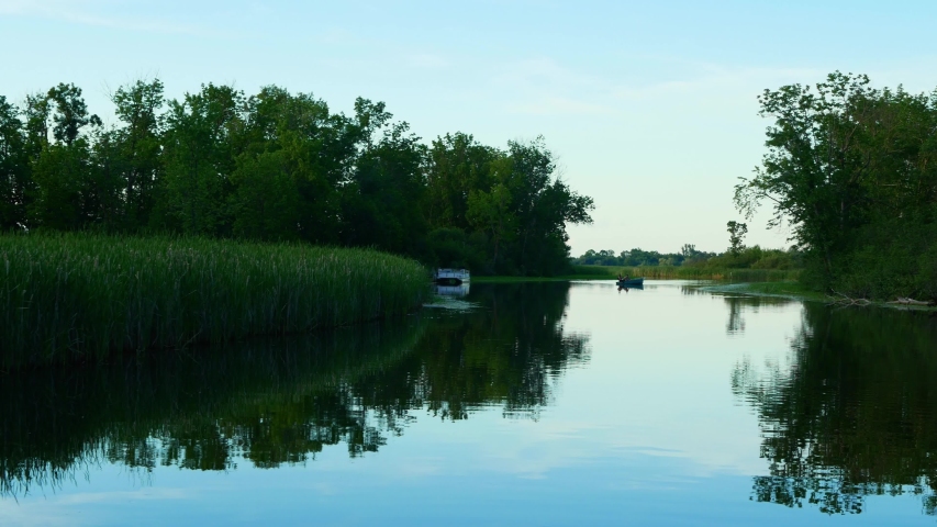 Boating on the beautiful Mississippi River in Bemidji Minnesota near the headwaters where it still flows north, in a clip with a boat and docked pontoon downstream in early evening.
