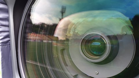 A detailed shot of a tv video camera big front lens. The glass reflects the football stadium.