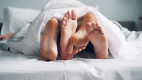 Mans and womans feet are moving under blanket caressing touching in bed on white sheets, people aare enjoying bedtime together. Relationship and body concept. - Powered by Shutterstock - Get 15% off with code: PIKWIZARD15