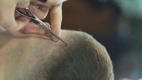 The barber styles client's haircut using sharp hair scissors and a little comb. It is a close up video of vertical orientation. The background is blurred.