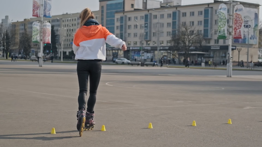 Young woman rides on roller skates and whirl in slow motion. Active woman skating outdoors in UHD