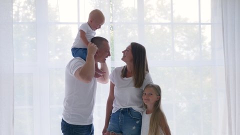 family of four stands in a white room against a large window