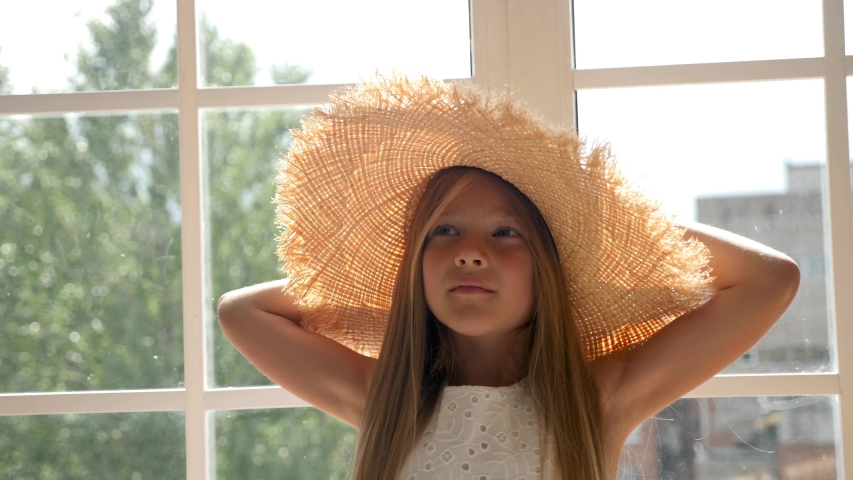 girl in a big straw hat and a white dress sitting on the window