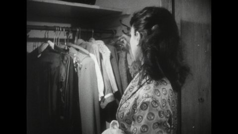 1940s: Brunette teenage girl in robe removes clothing from hangers in her closet. Girl takes clothes into another room and shuts the door. Blonde teenage girl continues sleeping in bed.
