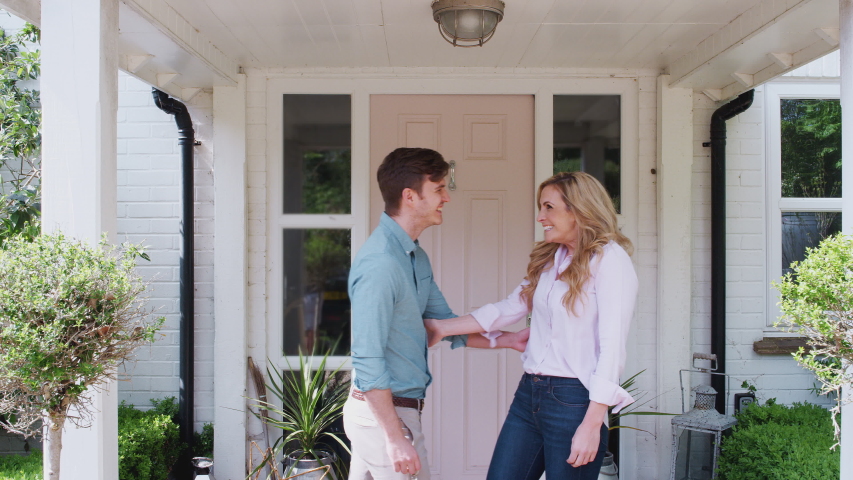Portrait Of Couple Holding Keys To New Home Standing Outside Front Door