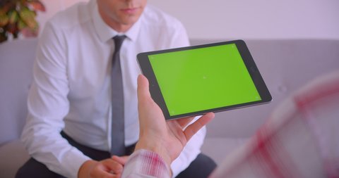 Closeup portrait of customer service manager talking to client holding tablet with green screen in office