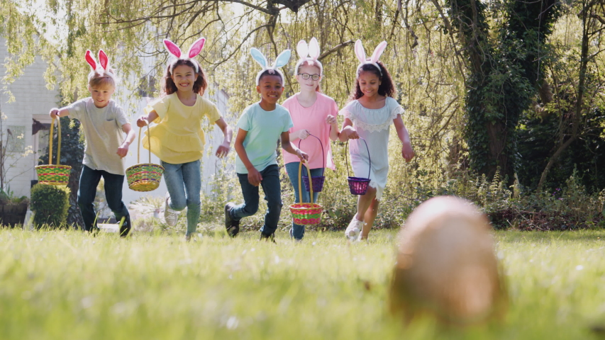 Group Of Children Wearing Bunny Ears Running To Pick Up Chocolate Egg On Easter Egg Hunt In Garden Royalty-Free Stock Footage #1035012059