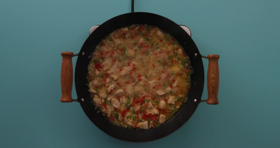 putting oil, stirring broth, vegetables, chicken stir fry, diced onions, rice and adding salt, pepper, red and green peppers in a skillet, 