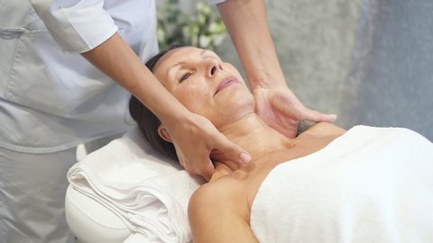 Charming and calm woman with closed eyes spending free time on relaxing procedure. Female lying on massage table enjoying health touch of professional in bright and light spa salon