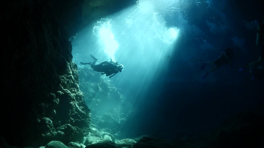 scuba divers underwater exploring the caves caverns and tunnels with sun beams and rays Royalty-Free Stock Footage #1035021821