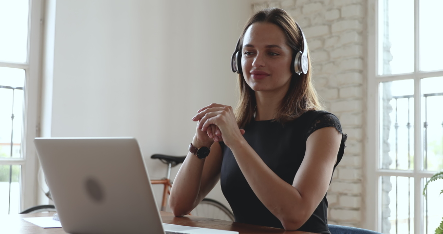 Smiling young business woman receptionist wear wireless headphone video conference calling on laptop computer talk by webcam in online chat, customer support service and online study teaching concept Royalty-Free Stock Footage #1035023864