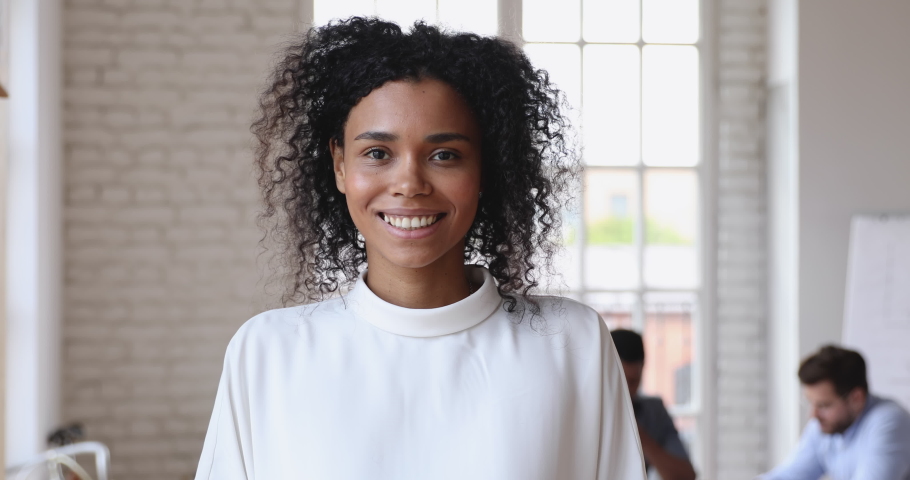 Smiling young african american female leader office worker intern standing in modern office looking at camera, happy mixed race employee business coach millennial professional hr close up portrait