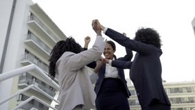 Cheerful young businesswomen outdoor. Low angle view of excited multiethnic female colleagues triumphing together on street. Success concept