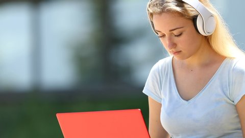 Concentrated girl wearing headphones using a red laptop outside in a campus